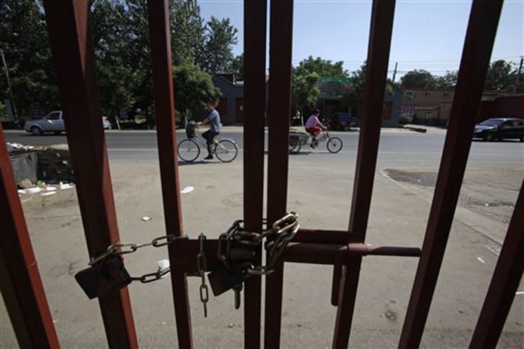 Residents cycle past on the outside of a locked exit to a gated village on the outskirts of Beijing on July 8.